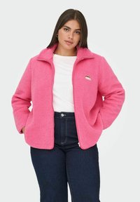 Kurtka z polaru w jaskrawym różowym kolorze, z wysokim kołnierzem i zamkiem z przodu. Posiada kieszenie po bokach oraz małą naszywkę z logo na piersi.