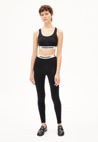 Zwarte sportbh met een brede witte merkband, gecombineerd met hoge zwarte legging. Beide gemaakt van glad, rekbaar materiaal.