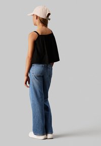 Top corto negro con tirantes finos, jeans de tiro alto azules y zapatillas blancas. Gorra rosa claro llevada al revés, mostrando un look casual.