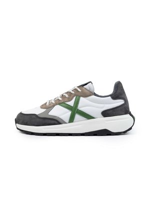 Zapatilla blanca con acentos en gris y verde, que presenta una combinación de materiales lisos y de ante, cierre de cordones y una suela de tracción texturizada.