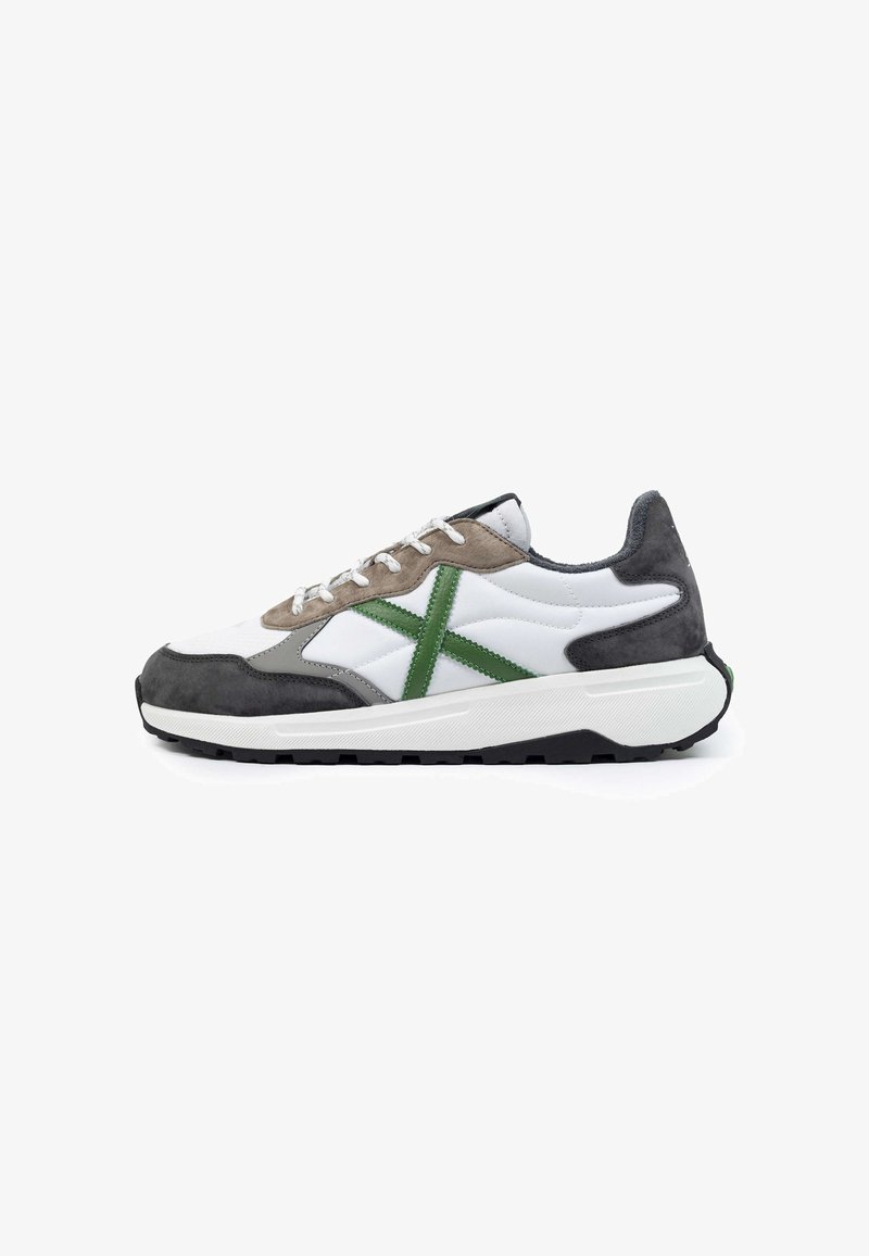 Zapatilla blanca con acentos en gris y verde, que presenta una combinación de materiales lisos y de ante, cierre de cordones y una suela de tracción texturizada.