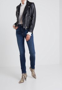 Chaqueta de cuero negra de motorista con cremalleras plateadas, vaqueros de tiro alto en azul y botines de piel de serpiente con puntera puntiaguda. Detalles de tejido texturizado visibles.