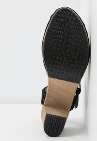 Sandale noire avec une semelle en caoutchouc texturé, un intersemelle en bois et des brides réglables. Présente un logo en relief sur la semelle pour une meilleure adhérence.