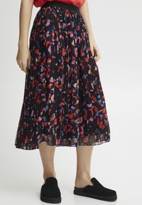 Een zwarte geplooide rok met een kleurrijk abstract patroon in rood, roze en blauw. De tailleband is zwart, gecombineerd met zwarte instapschoenen.