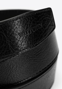 Cintura in pelle nera con superficie testurizzata, bordo liscio e marchio impresso. Il design è minimalista ed elegante.