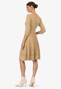 Abito a tre quarti con maniche, lungo fino al ginocchio, in maglia beige chiaro con finitura testurizzata e dettagli perforati all'orlo, abbinato a stivali alla caviglia beige.