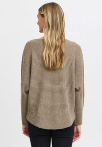 Hellbrauner, gestrickter Pullover mit lockerer Passform und gerippter Textur; verfügt über einen abgerundeten Saum und überschnittene Schultern, kombiniert mit schwarzen Hosen.