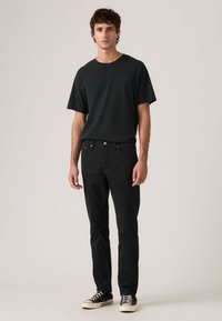 Μαύρο βαμβακερό T-shirt με στρογγυλή λαιμόκοψη, συνδυασμένο με μαύρο τζιν και μαύρα αθλητικά παπούτσια. Απλός σχεδιασμός με εφαρμοστή σιλουέτα.