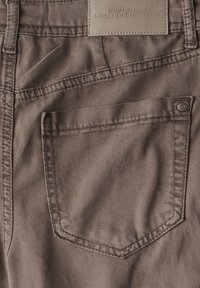 Bakfickan på bruna denimjeans med synlig söm, en metallnitar och en läderlapp med texten "Street One Denim Atelier."