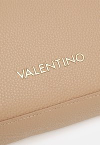 Bežinė odinė rankinė su tekstūruota paviršiumi, įspaustu auksiniu "Valentino" logotipu ir kontrastingomis siūlėmis aplink kraštus.