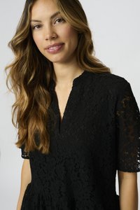 Top in pizzo nero con motivi floreali, maniche corte con bordi ondulati e scollatura a V. Tessuto testurizzato con un effetto a strati.