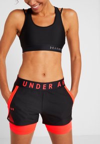 Svart sport-bh med en grå logotyp och svarta träningsshorts med röd midja och sidodetaljer. Slät, elastisk tyg.