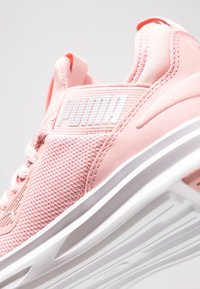 Primo piano di una sneaker rosa Puma con tomaia in mesh, colletto imbottito e dettagli della suola bianca.