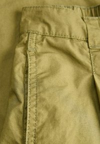 Gros plan sur un tissu brun clair froissé avec des coutures verticales et horizontales, probablement une partie de la ceinture et de la poche d'un vêtement.