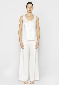 Biała, bezrękawnikowa bluzka w połączeniu z szerokimi spodniami, obie z lekkiego, strukturalnego materiału. Sandały z paskami na kostkach. Prosty krój.