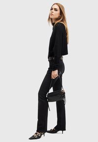 Maglione nero croppato e jeans neri a vita alta, abbinati a scarpe nere a punta con dettagli in oro sulle fibbie. Borsa a spalla nera.