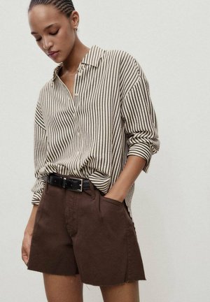 Gestreepte beige en zwarte button-up shirt, ingestopt in bruine shorts met zakken en een rafelige zoom, vastgemaakt met een zwarte riem.