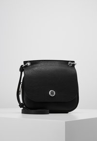 Black leather crossbody bag with a textured finish, flap closure, silver hardware, and a circular logo accent. Adjustable strap included.