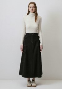 Jupe maxi en denim noir avec des poches latérales, coutures blanches contrastantes et fermeture à boutons à l'avant, associée à un col roulé ajusté couleur crème.