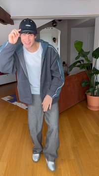 Grå fleecejakke med blå detaljer, hvit t-skjorte, gråstripete bukser og sølvfargede joggesko. Svart caps med teksten "FORMER". Innendørs setting.