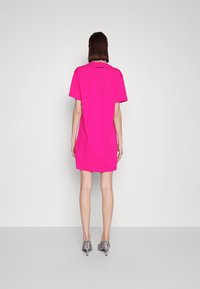 Rosa Baumwoll-T-Shirt-Kleid mit kurzen Ärmeln, einem runden Ausschnitt und Seitenschlitzen. Getragen mit schwarz-weiß gestreiften High Heels.