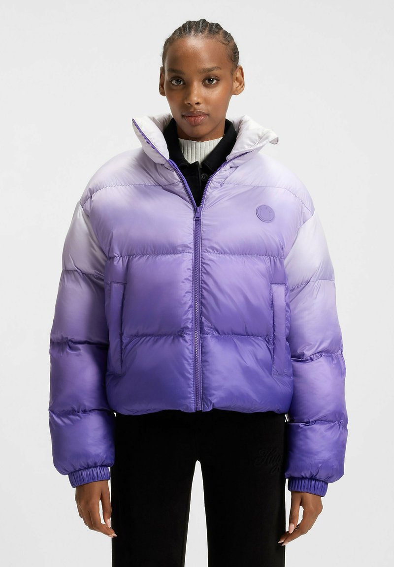 Lilla gradient puffer jakke med høj krave, lynlåslukning og elastiske manchetter. Har et patch-logo på brystet og en blød tekstur.