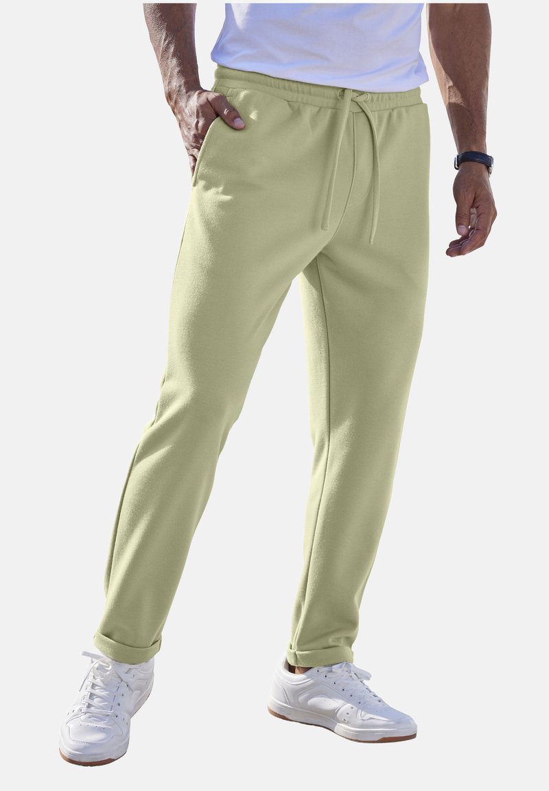 Helles grünes Fleece-Jogginghose mit elastischem Bund und verstellbarem Kordelzug; verfügt über Seitentaschen und schmal zulaufende Bündchen. Kombiniert mit weißen Sneakern.