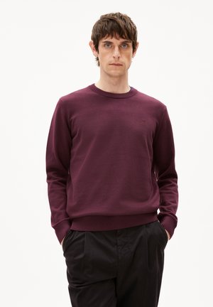 Bordeaux crewneck sweatshirt gemaakt van een gladde stof, met ribgebreide manchetten en taille. Klein logo-accent op de borst, gecombineerd met zwarte broek.