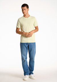 T-shirt di cotone verde pallido a maniche corte, con un piccolo logo azzurro. Indossata con jeans in denim azzurro chiaro e sneakers bianche.