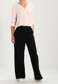 Blusa rosa chiaro a maniche lunghe con scollo a V; abbinata a pantaloni neri a gamba larga; sneakers bianche completano il look. Tessuto morbido, design casual.