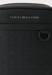 Borsa nera con motivo intrecciato, sezione superiore liscia e dettaglio hardware circolare. Logo inciso nella parte superiore.