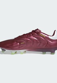 Scarpa da calcio color mogano in materiale sintetico testurizzato, con punta arrotondata, lacci e tallone argentato a contrasto. Presenta tacchetti con sfumature verdi.