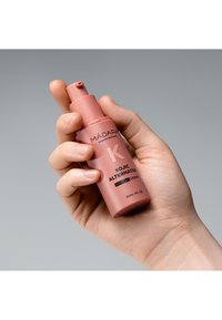 Bottiglia di plastica rosa con tappo a pompa, etichettata "Siero di pigmento alternativo Kojic." Tenuta in mano, dimensione 30ml visibile. Finitura opaca.