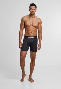 Shorts de boxeur noirs en tissu extensible avec une ceinture logo. Le design est ajusté, de longueur mi-cuisse et unis sans motifs.
