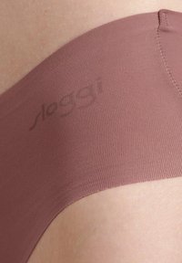 Biancheria intima senza cuciture di colore rosa chiaro con un tessuto testurizzato a coste. Il nome del marchio è stampato in modo discreto, visibile vicino al bordo.