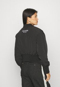 Black bomber jacket with ribbed cuffs and hem, featuring the "HILFIGER NEW YORK" logo embroidered on the back. Smooth fabric texture.