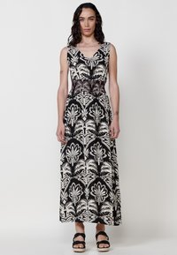 Robe maxi en noir et crème avec motif floral. Dotée d'un décolleté en V, taille ajustée avec des détails délicats et une jupe fluide.
