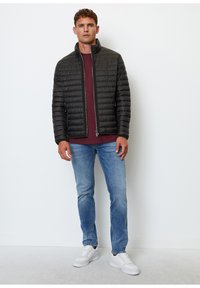 Chaqueta de plumas negra con cuello alzado, cierre de cremallera, cintura acanalada, llevada sobre una camisa burdeos, combinada con jeans azules y zapatillas blancas.
