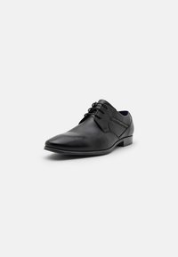 Chaussure habillée en cuir noir avec un bout pointu, fermeture à lacets et un petit talon carré. Présente une texture lisse et des détails de couture subtils.
