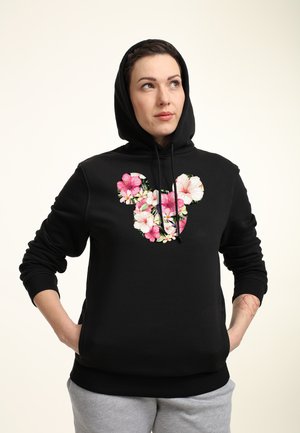 Sort hættetrøje med blomsterdesign i pink og hvid på fronten, med hætte og ribbede manchetter, stylet med grå svedbukser.
