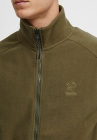 Olivgrüne Fleecejacke mit hohem Kragen und durchgehendem Reißverschluss. Mit gesticktem Logo und strukturiertem Stoff für Wärme.