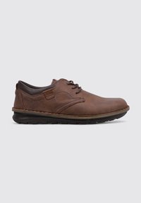 Chaussure en cuir marron avec un bout arrondi, un laçage classique et une semelle rembourrée. Présente des coutures discrètes et un accent texturé sur les côtés.