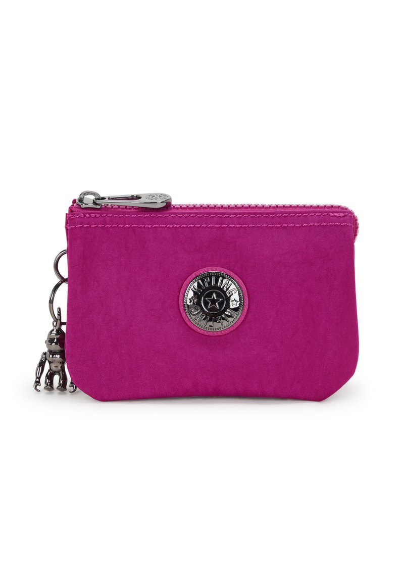 Portafoglio fucsia con zip realizzato in materiale morbido, caratterizzato da un emblema circolare in argento e un charm metallico a forma di piccola figura appeso.