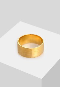 Wide gold band ring with a brushed finish resting on a white surface at an angle.