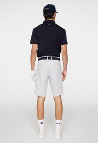 Mörkblå polo tröja, grå shorts, vita strumpor med logotyp och golfhandske. Outfiten har en enkel design med en sportig look.