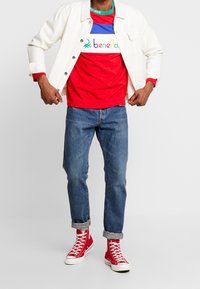 Camisa de rayas rojas y azules debajo de una chaqueta de mezclilla blanca, combinada con jeans azules arremangados y zapatillas altas rojas.