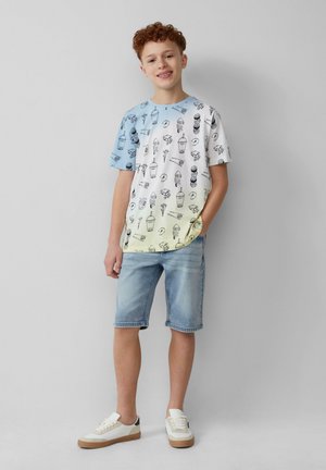 Korte mouw t-shirt met een blauwe gradient en zwarte illustraties van ijs en desserts. Gepaard met lichte denim shorts en witte sneakers.