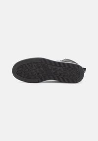 Suela de zapato deportivo negro con goma texturizada para agarre, que presenta un logotipo de marca prominente y un patrón geométrico para tracción.