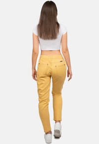 Pantalons jaunes à taille élastique avec une coupe fuselée, dotés de deux poches arrière et portés avec des baskets blanches.