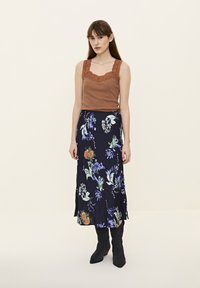 Top cu bretele maro, cu dantelă la margine, asortat cu o fustă maxi florală cu fundal albastru închis și modele florale multicolore, completat cu cizme negre.